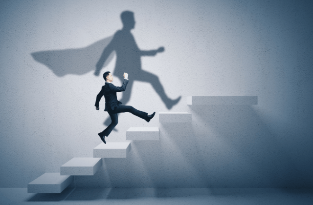 Business person walking upstairs with superhero shadow on wall